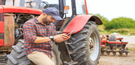 Farmer with smartphone leaning on tractor